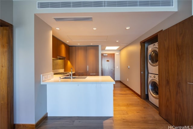 kitchen featuring light hardwood / wood-style floors, kitchen peninsula, sink, and stacked washer and clothes dryer