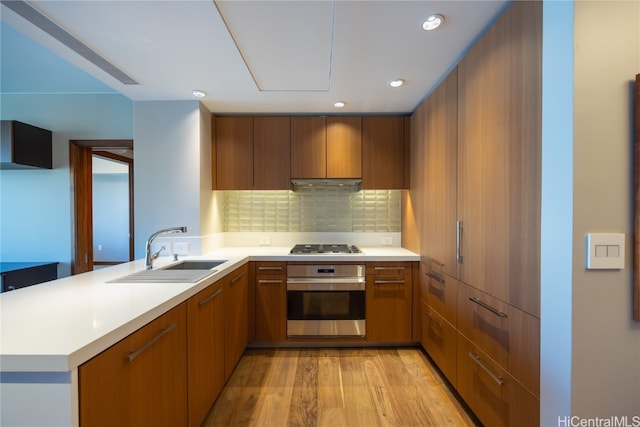 kitchen featuring sink, backsplash, kitchen peninsula, light hardwood / wood-style floors, and appliances with stainless steel finishes