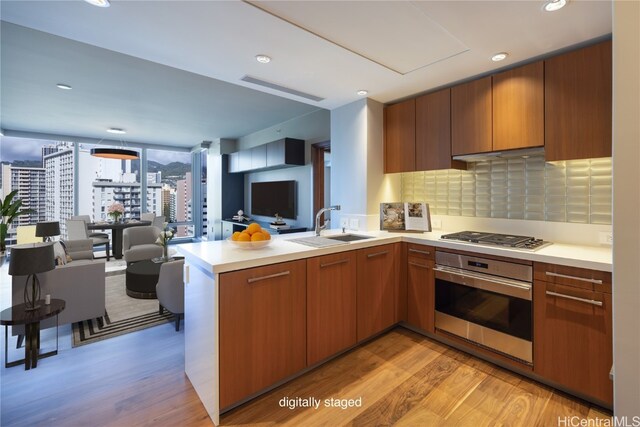 kitchen with sink, decorative backsplash, appliances with stainless steel finishes, light hardwood / wood-style floors, and kitchen peninsula