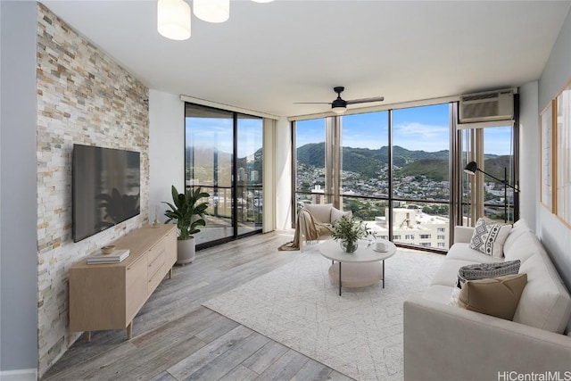 living room featuring an AC wall unit, a healthy amount of sunlight, a wall of windows, and light hardwood / wood-style flooring