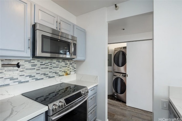 kitchen featuring hardwood / wood-style floors, backsplash, stacked washer and clothes dryer, light stone counters, and stainless steel appliances