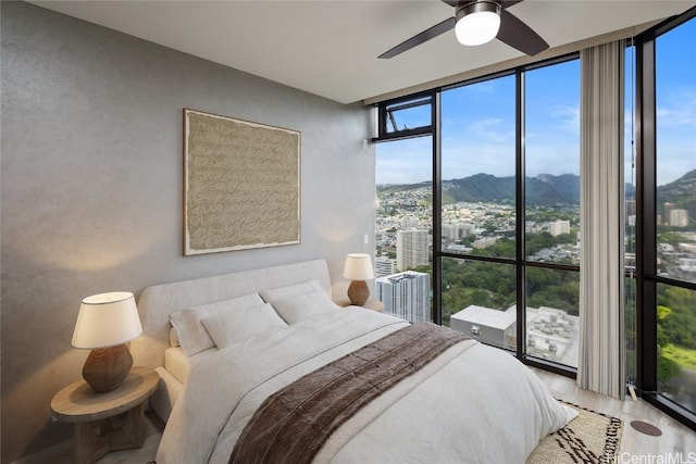 bedroom featuring light hardwood / wood-style flooring, a mountain view, a wall of windows, and ceiling fan