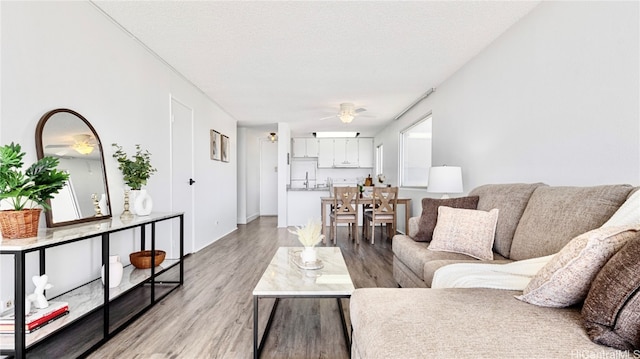 living room with a textured ceiling, light wood-type flooring, and ceiling fan