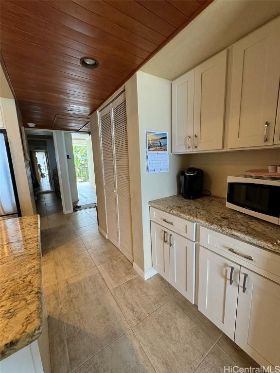 kitchen featuring light stone counters, light tile patterned floors, wood ceiling, white cabinets, and baseboards