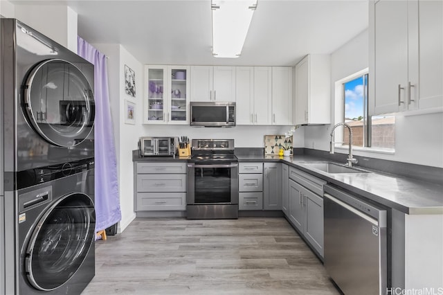 kitchen featuring stacked washer and dryer, sink, light wood-type flooring, appliances with stainless steel finishes, and white cabinetry