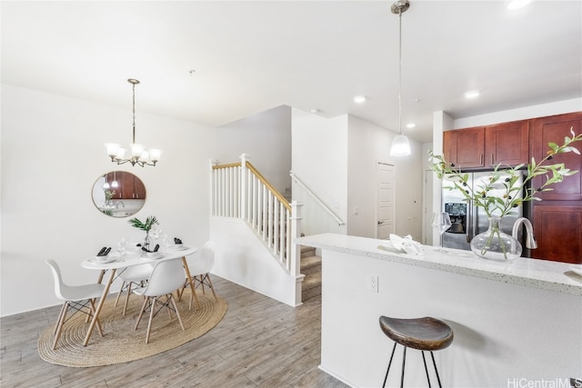 kitchen with light stone counters, an inviting chandelier, stainless steel refrigerator with ice dispenser, light hardwood / wood-style flooring, and decorative light fixtures