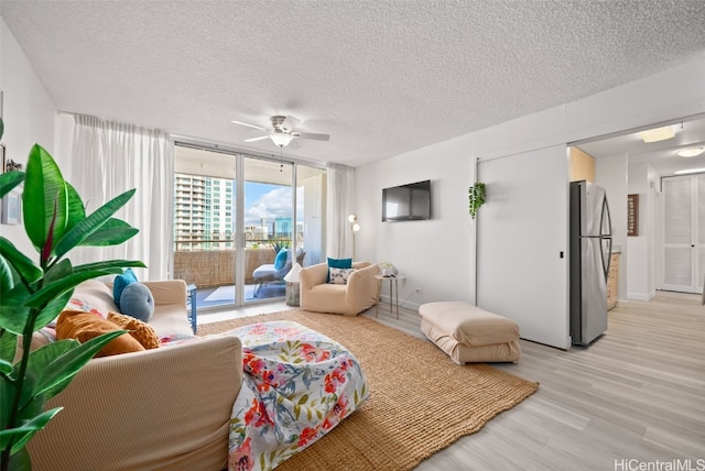 living room with a wall of windows, ceiling fan, a textured ceiling, and light wood-type flooring