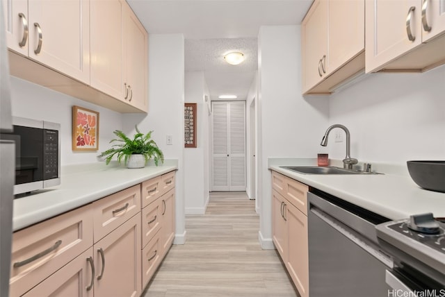 kitchen featuring appliances with stainless steel finishes, a textured ceiling, light hardwood / wood-style floors, and sink