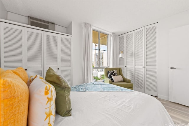 bedroom featuring multiple closets, light hardwood / wood-style flooring, a wall mounted air conditioner, and a textured ceiling