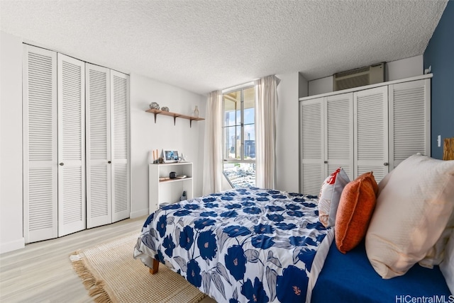 bedroom featuring two closets, a textured ceiling, and light wood-type flooring