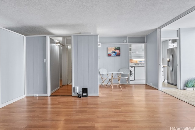 unfurnished living room with washer / dryer, light wood-type flooring, and a textured ceiling