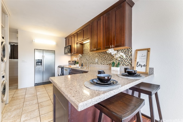 kitchen featuring light tile patterned flooring, sink, appliances with stainless steel finishes, a kitchen bar, and decorative backsplash