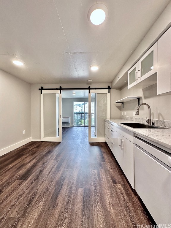 kitchen with a barn door, sink, stainless steel dishwasher, dark hardwood / wood-style floors, and white cabinetry