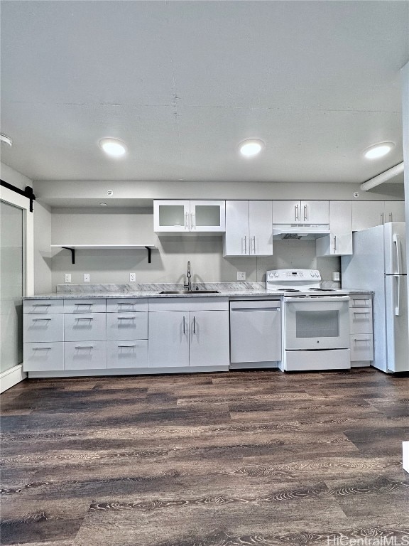 kitchen with a barn door, dark hardwood / wood-style flooring, sink, white cabinets, and white appliances