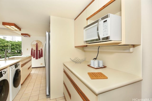 kitchen with white cabinets, washing machine and dryer, sink, stainless steel refrigerator, and light tile patterned floors