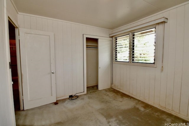 unfurnished bedroom with wooden walls, a closet, and light colored carpet