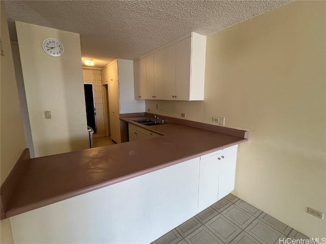 kitchen with a textured ceiling, kitchen peninsula, sink, and white cabinets