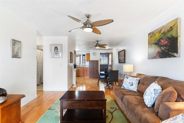 living room with light wood finished floors, baseboards, and a ceiling fan