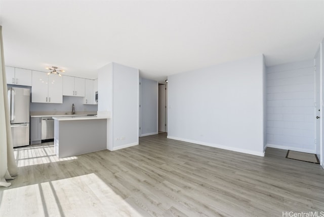 kitchen with kitchen peninsula, sink, stainless steel refrigerator, white cabinetry, and light hardwood / wood-style flooring