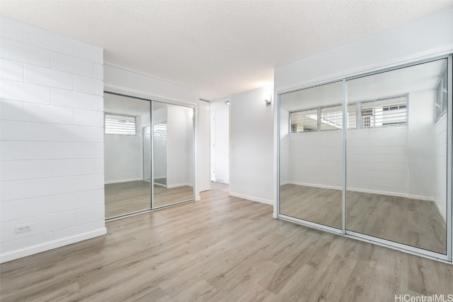 unfurnished bedroom with multiple windows, a textured ceiling, a closet, and light hardwood / wood-style flooring