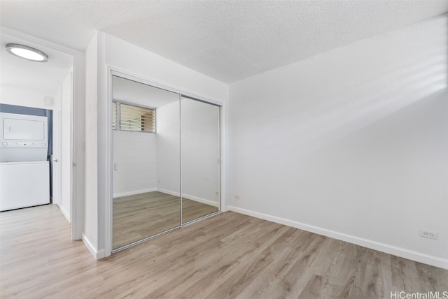 unfurnished bedroom featuring light hardwood / wood-style flooring, a textured ceiling, stacked washer and clothes dryer, and a closet