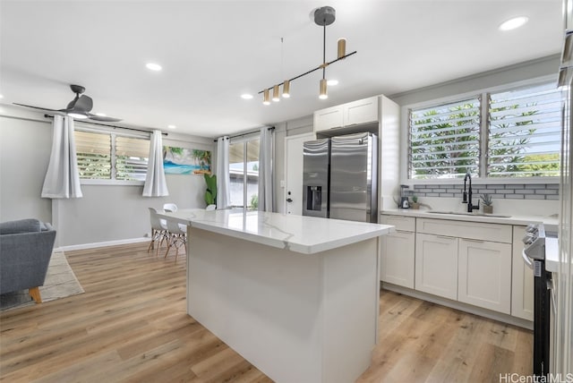 kitchen featuring stainless steel appliances, white cabinetry, hanging light fixtures, sink, and light hardwood / wood-style floors