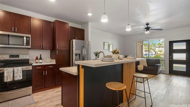 kitchen with a center island with sink, light hardwood / wood-style flooring, decorative light fixtures, a kitchen bar, and stainless steel appliances