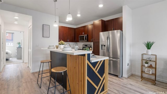 kitchen with decorative light fixtures, light wood-type flooring, a breakfast bar area, and appliances with stainless steel finishes