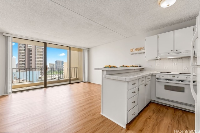 kitchen with expansive windows, white cabinets, tile counters, light wood-type flooring, and electric range