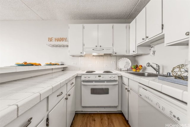 kitchen with tile counters, wood-type flooring, white cabinets, sink, and white appliances