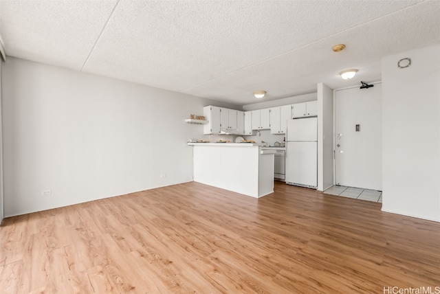 kitchen with white fridge, white cabinetry, a textured ceiling, kitchen peninsula, and light hardwood / wood-style flooring