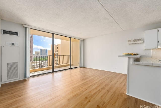 unfurnished living room featuring a textured ceiling, a wall of windows, and light hardwood / wood-style flooring