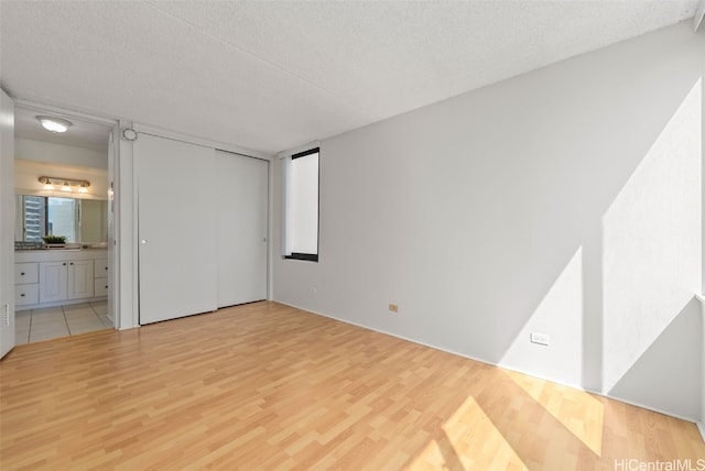 unfurnished bedroom featuring connected bathroom, a textured ceiling, and hardwood / wood-style flooring