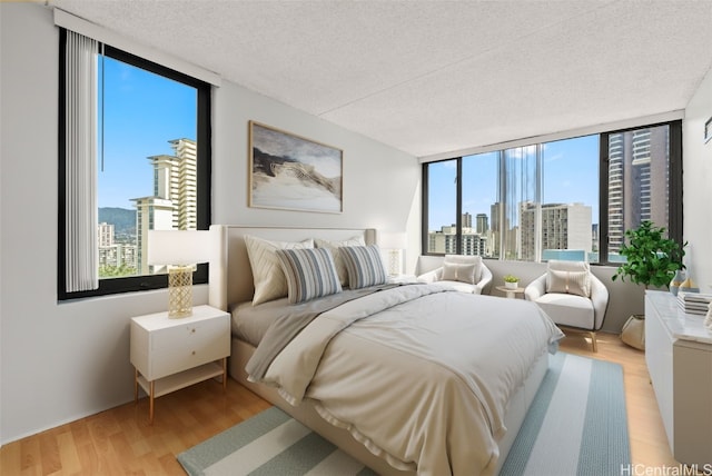 bedroom featuring a textured ceiling, a wall of windows, light hardwood / wood-style floors, and multiple windows