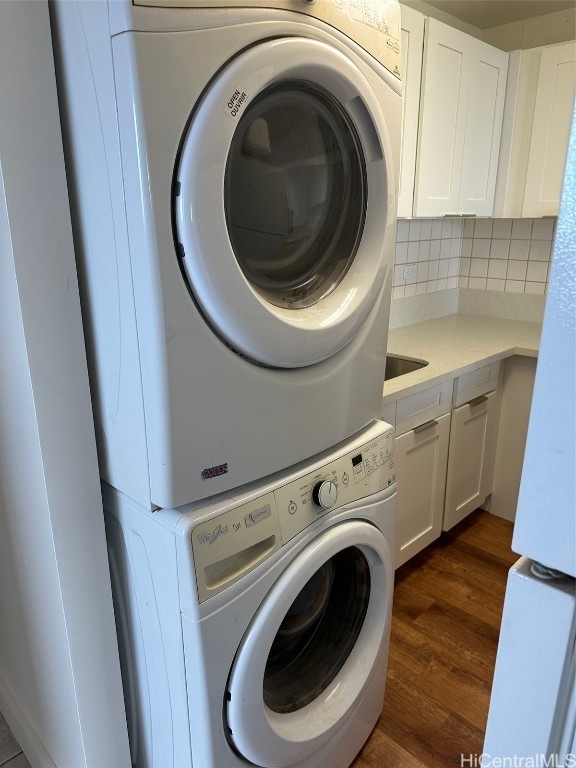 laundry room featuring dark wood-type flooring, cabinets, and stacked washer / drying machine