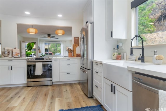 kitchen featuring white cabinetry, decorative light fixtures, appliances with stainless steel finishes, and light hardwood / wood-style flooring