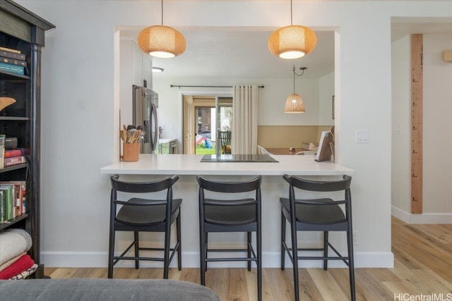 kitchen with a kitchen breakfast bar, light hardwood / wood-style floors, hanging light fixtures, and stainless steel refrigerator