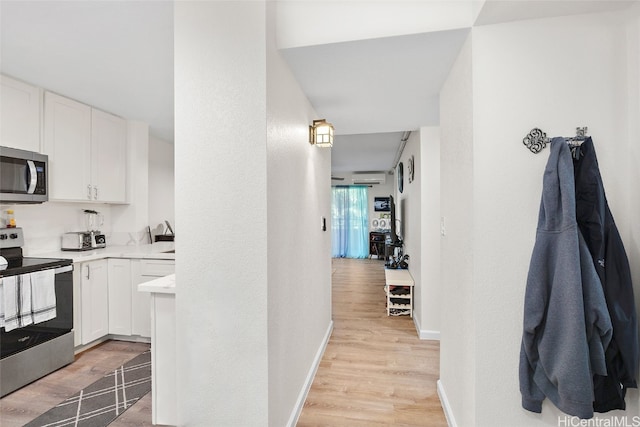 interior space featuring white cabinets, stainless steel appliances, light hardwood / wood-style flooring, and a wall unit AC