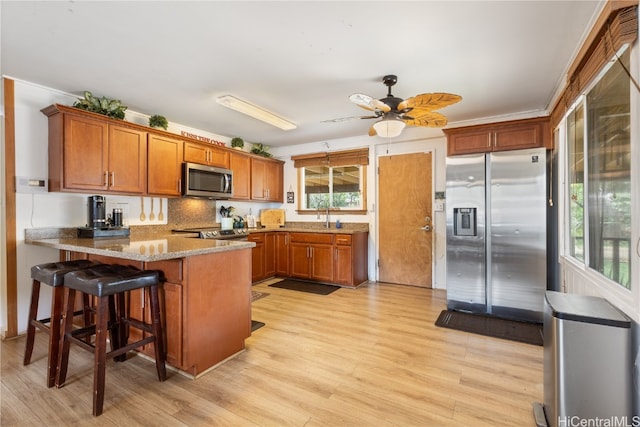 kitchen with kitchen peninsula, ceiling fan, a breakfast bar, light wood-type flooring, and appliances with stainless steel finishes