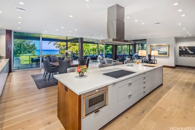 kitchen with a large island, expansive windows, black electric cooktop, white cabinets, and light wood-type flooring