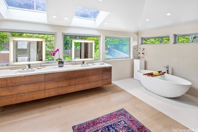 bathroom featuring vaulted ceiling with skylight, vanity, wood-type flooring, and a tub to relax in