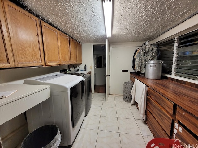 washroom featuring a textured ceiling, washing machine and dryer, cabinets, and light tile patterned floors