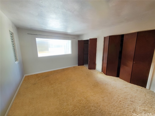 unfurnished bedroom featuring a textured ceiling, light carpet, and two closets