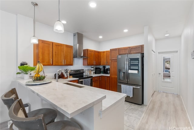 kitchen featuring stainless steel appliances, wall chimney range hood, pendant lighting, sink, and kitchen peninsula