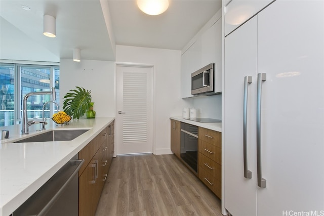 kitchen with light hardwood / wood-style floors, stainless steel appliances, sink, light stone countertops, and white cabinetry