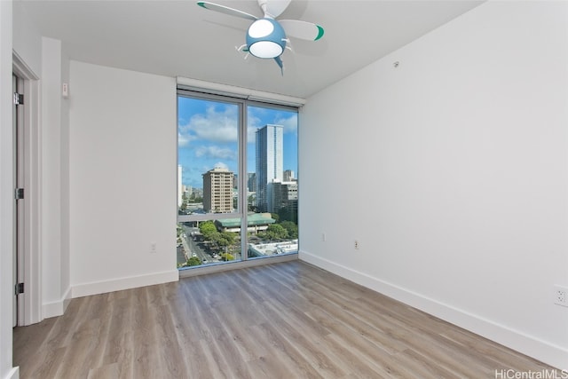 spare room with a wall of windows, light hardwood / wood-style floors, and ceiling fan