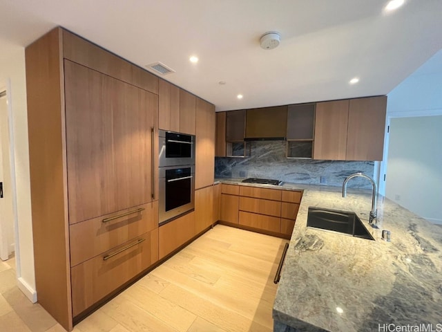 kitchen with sink, gas stovetop, light stone counters, backsplash, and light wood-type flooring