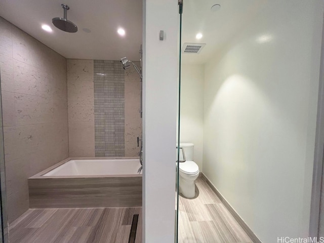 bathroom with hardwood / wood-style flooring, tiled shower / bath combo, and toilet