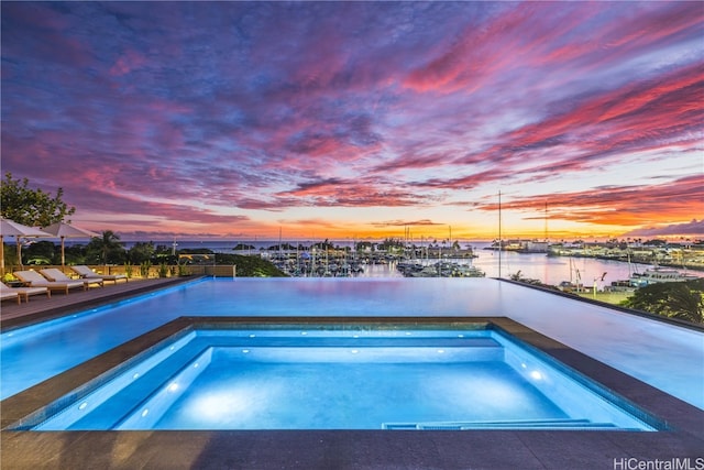 pool at dusk with a water view and an in ground hot tub