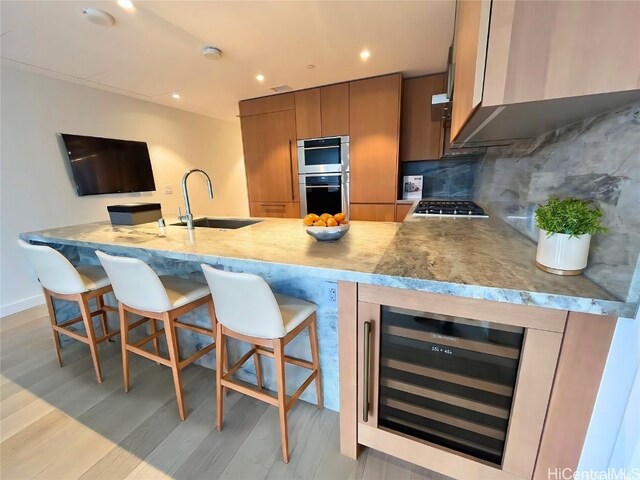 kitchen featuring a kitchen breakfast bar, tasteful backsplash, beverage cooler, sink, and light hardwood / wood-style floors